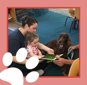 Caregiver and toddler reading to a brown dog