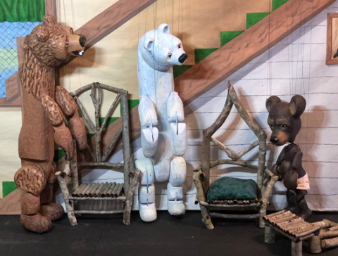 Three puppet bears next to their chairs.